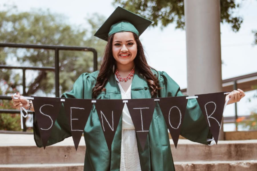 Girl in graduation cap and and gown holding a sign that says senior
